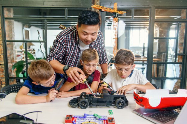 male-electronic-engineer-with-european-school-children-working-smart-school-lab-testing-model-radio-controlled-electric-car_141188-4965